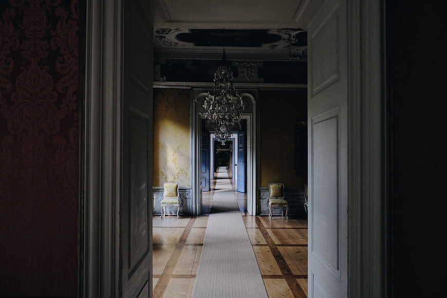 Long ornate hallway with chandeliers and vintage chairs