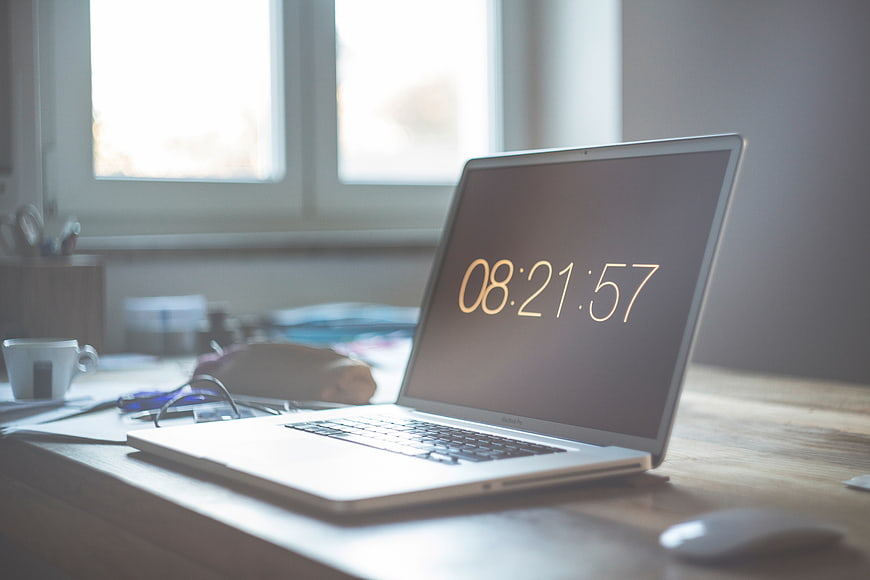 Laptop on wooden desk showing morning time 08:21:57