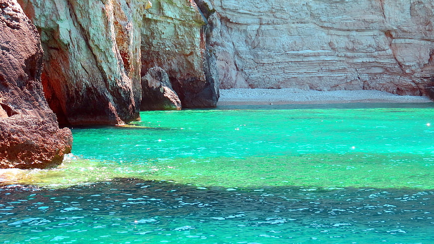 Vibrant turquoise sea water in a rocky cove with layered cliffs