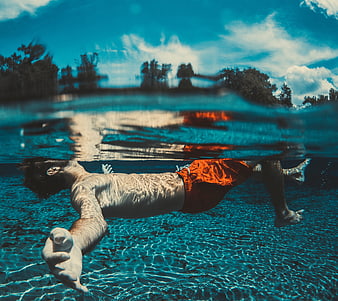 Man floating underwater in pool with split level view