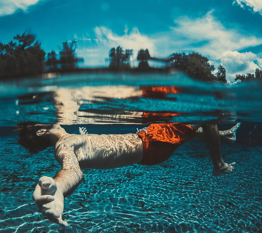 Man floating underwater in pool with split level view