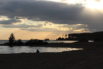 Silhouette of person sitting on beach at sunset with dramatic clouds
