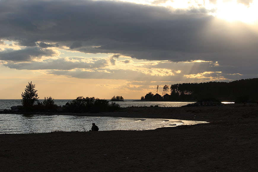 Silhouette of person sitting on beach at sunset with dramatic clouds