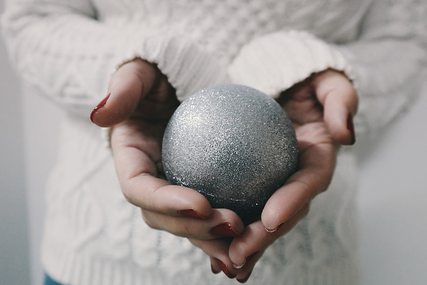 Woman holding silver glitter Christmas ornament in white sweater
