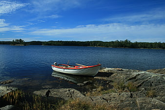 White and red boat moored on rocky lake shore