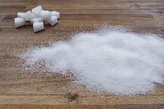 Granulated sugar and sugar cubes on wooden table