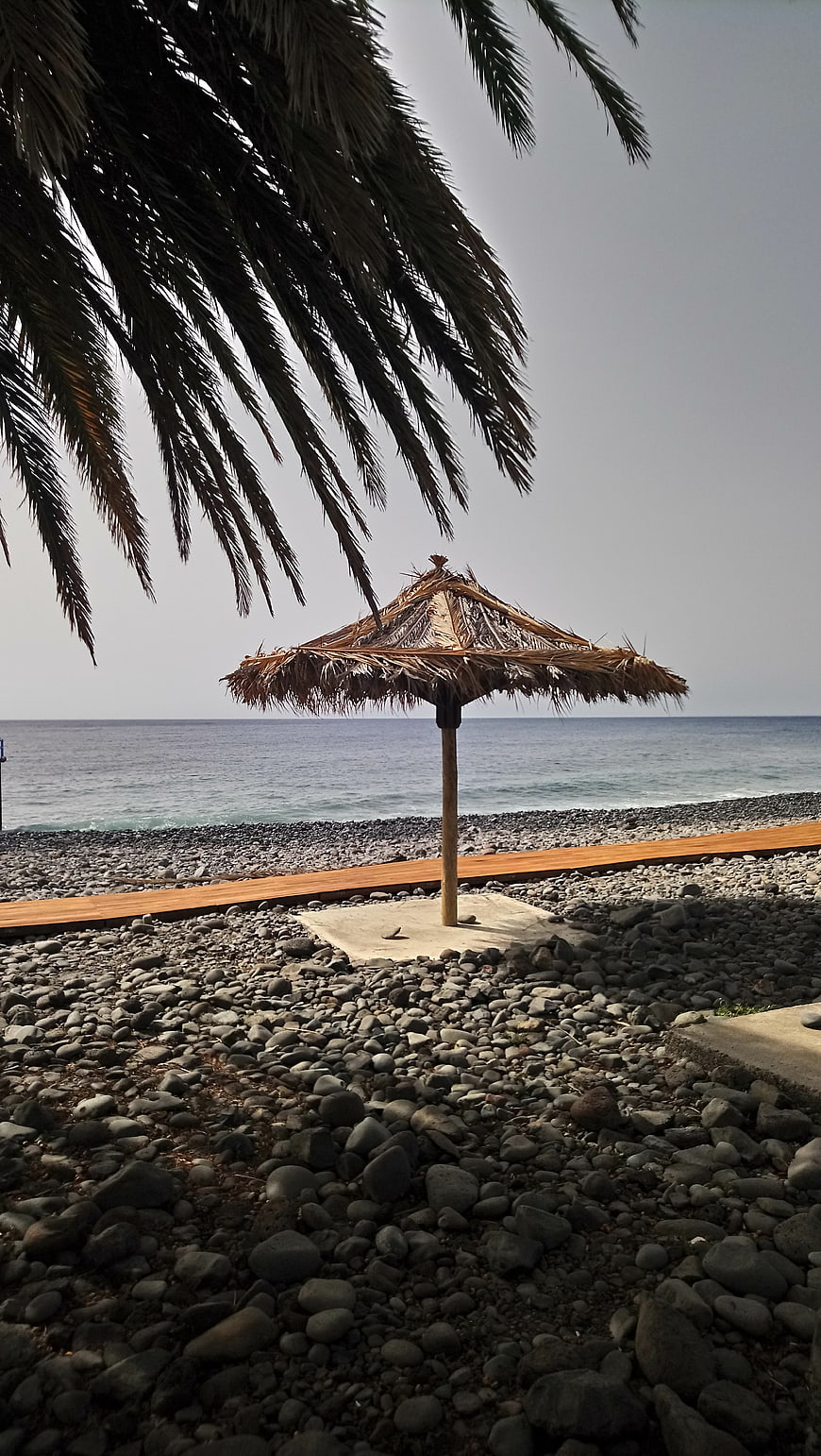 Thatched Beach Umbrella on Rocky Shore with Palm Leaves