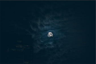 Full moon glowing through dark clouds at night