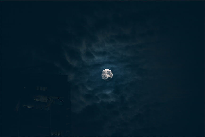 Full moon glowing through dark clouds at night