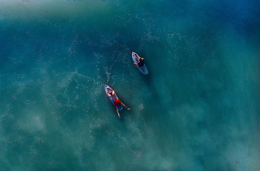 Aerial view of two men surfing in turquoise ocean water