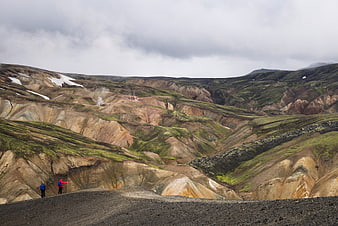 Hikers exploring colorful volcanic landscape with snow patches
