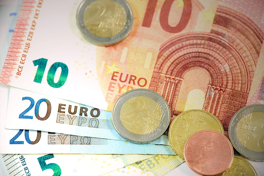 Euro banknotes and coins scattered on white background
