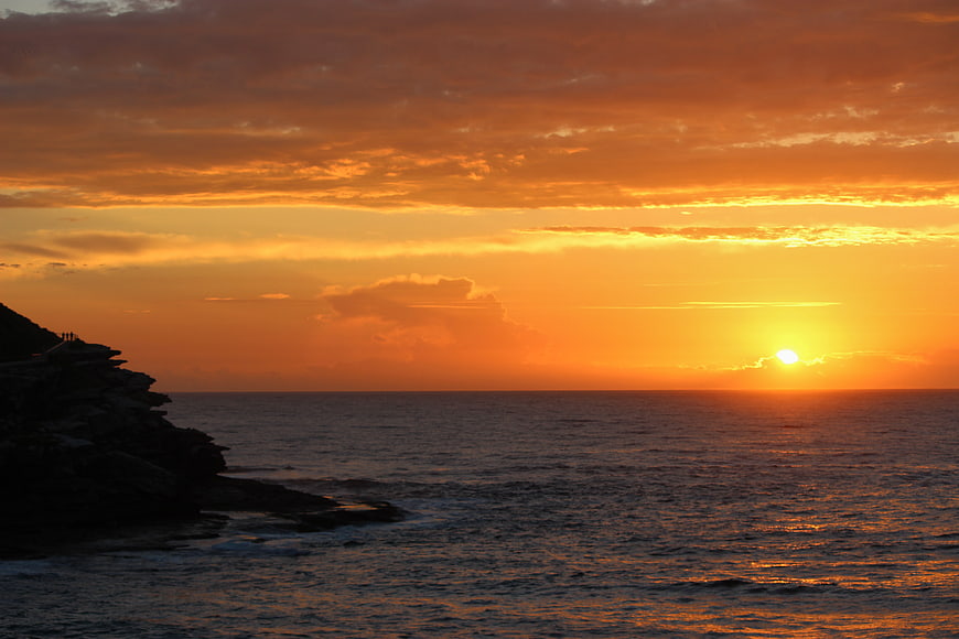 Dramatic Orange Sunset Over Ocean with Silhouetted Cliff