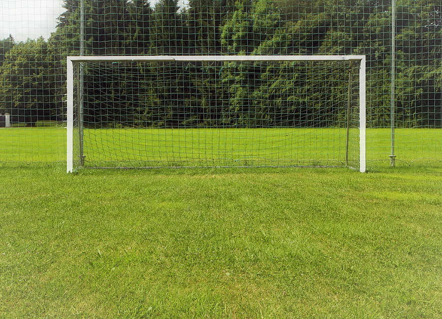 Empty soccer goal on green grass field with forest background