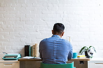 Man Sitting at Desk Facing White Brick Wall
