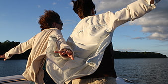 Couple with arms outstretched on boat at sunset
