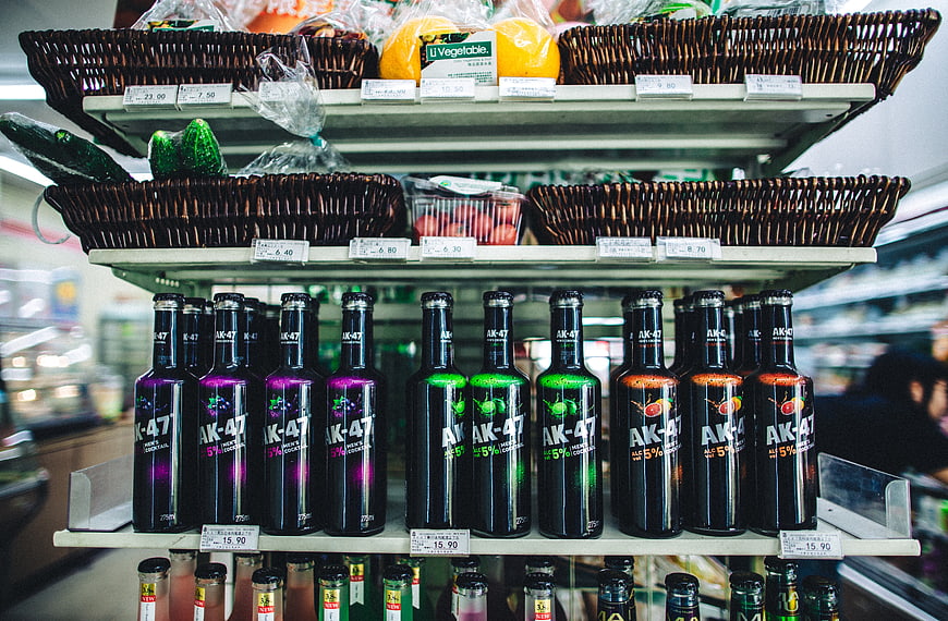 Colorful AK-47 cider bottles on supermarket shelf with fresh produce