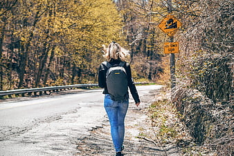Woman with backpack walking down rural road in autumn