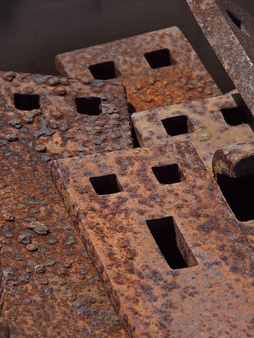 Close-up of heavily rusted metal blocks with square holes