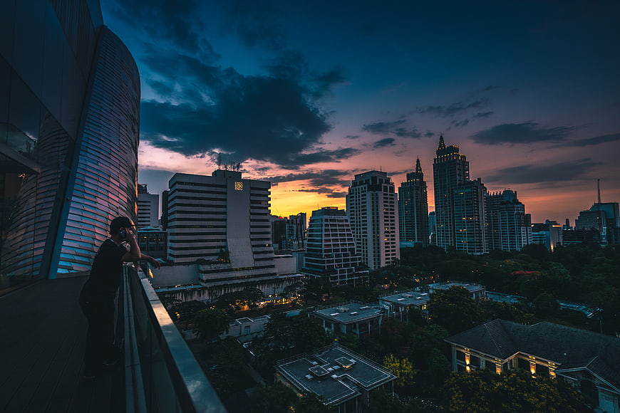 Man on Balcony Overlooking City Skyline at Sunset