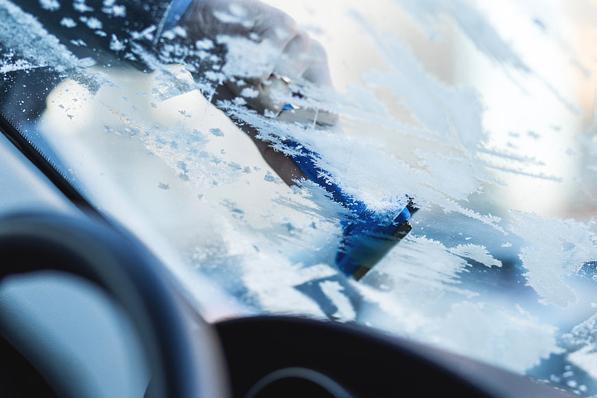 Close-up of hand scraping ice off car windshield in winter