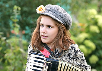 Young female folk musician playing accordion outdoors in vintage hat