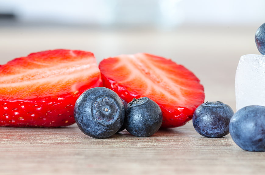 Fresh sliced strawberries and blueberries with ice on wood