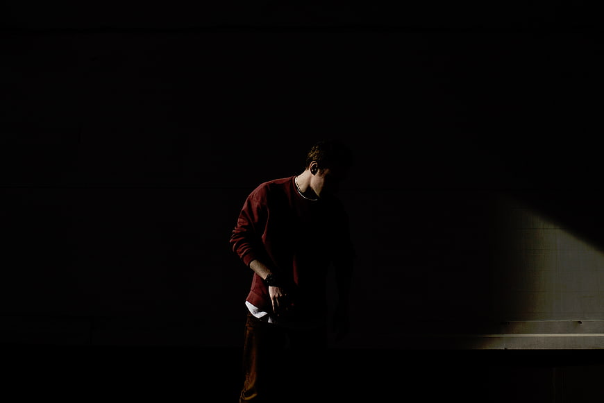 Man in Red Sweater Standing in Dark Room with Spotlight