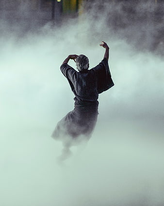 Senior man dancing in thick fog with arms raised