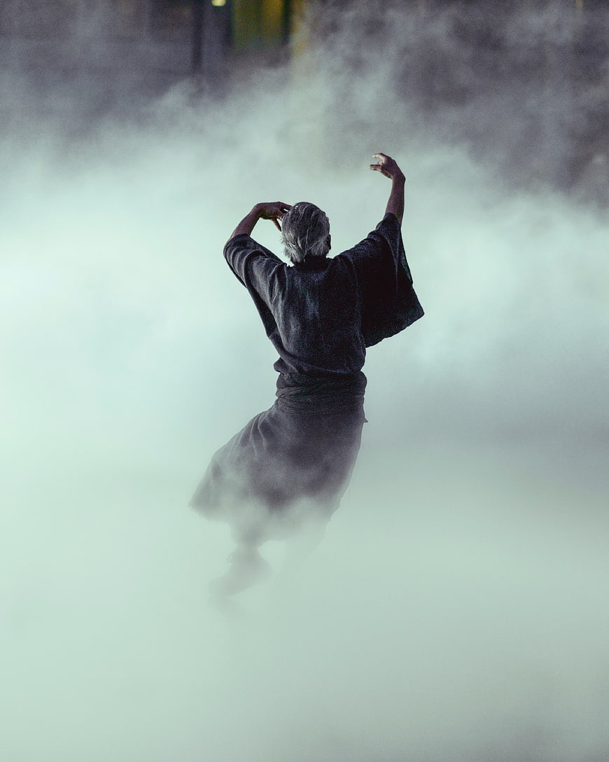 Senior man dancing in thick fog with arms raised