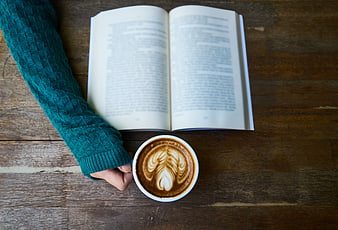 Flat lay of latte art coffee and open book on wooden table