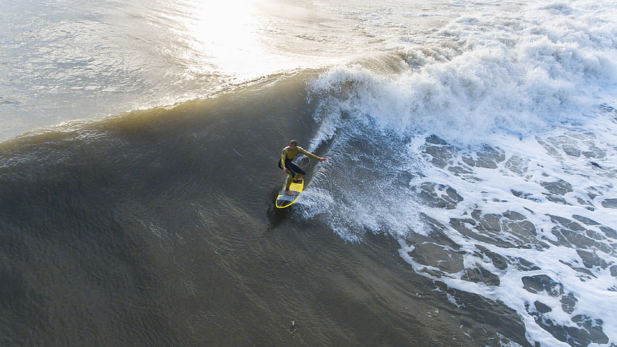 Aerial view of surfer riding a wave on a yellow surfboard