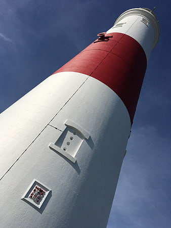 Low angle view of red and white striped lighthouse against blue sky