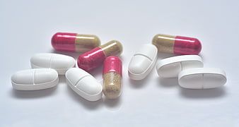 Assorted White Tablets And Pink Capsules On White Background