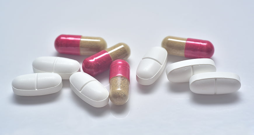 Assorted White Tablets And Pink Capsules On White Background