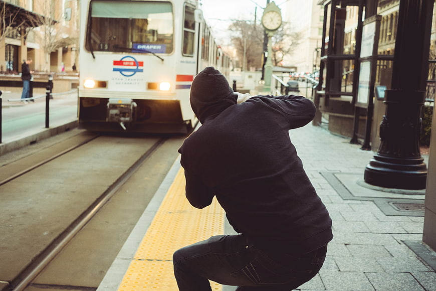 Man in Hoodie Crouching on Train Platform