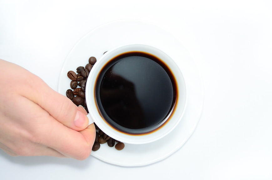 Top View Hand Holding Cup of Black Coffee with Beans