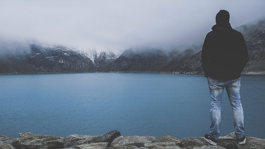 Man standing on rocks overlooking misty mountain lake