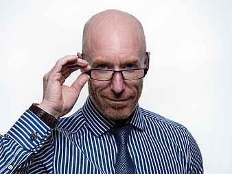 Bald man in striped shirt adjusting glasses against white background