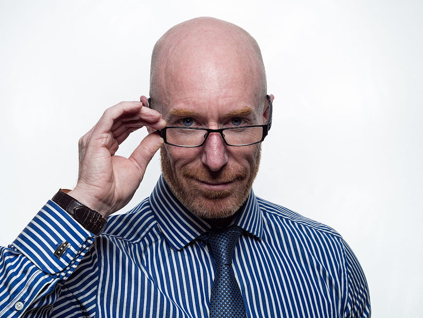 Bald man in striped shirt adjusting glasses against white background