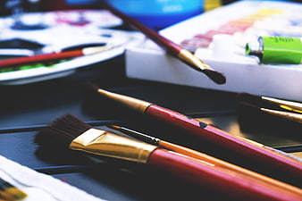 Close-up of red and gold paint brushes on a dark surface