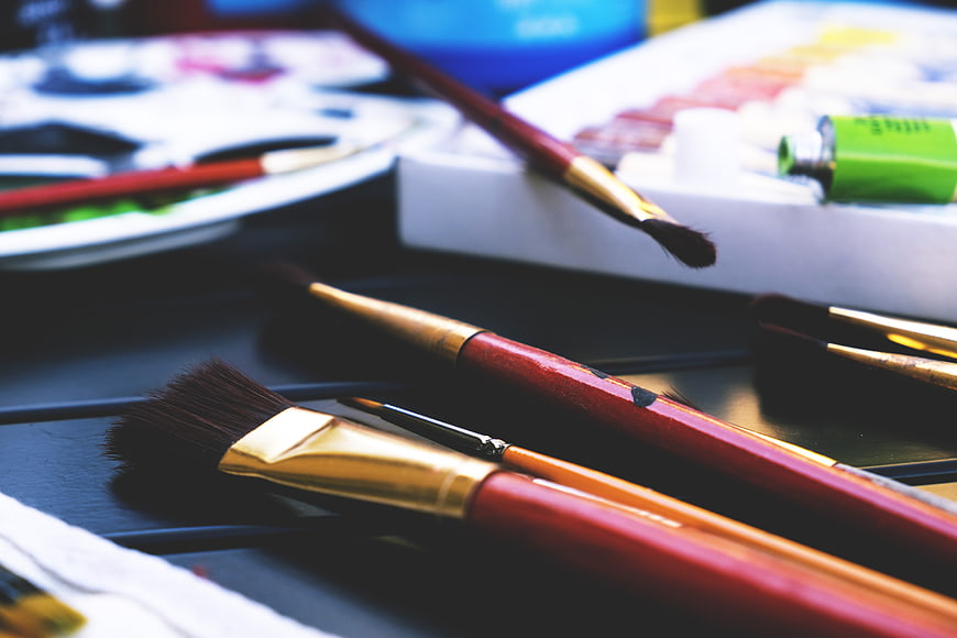 Close-up of red and gold paint brushes on a dark surface