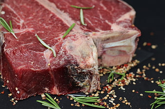Raw T-Bone Steak With Rosemary Sprigs And Seasoning On Dark Surface