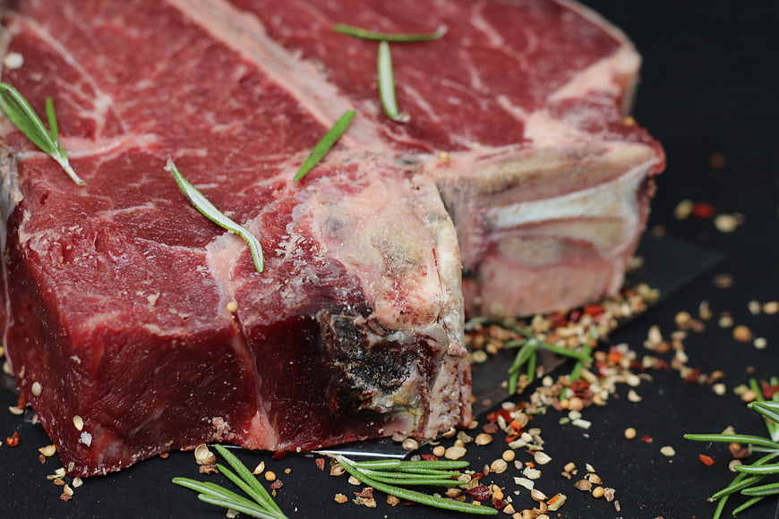 Raw T-Bone Steak With Rosemary Sprigs And Seasoning On Dark Surface