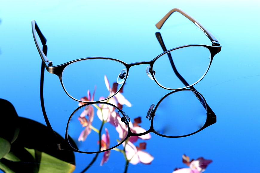 Black Eyeglasses on Blue Surface with Flower Reflection