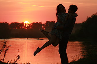 Romantic couple silhouette at sunset by a calm lake