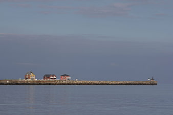 Serene coastal pier with houses and lighthouse at dusk