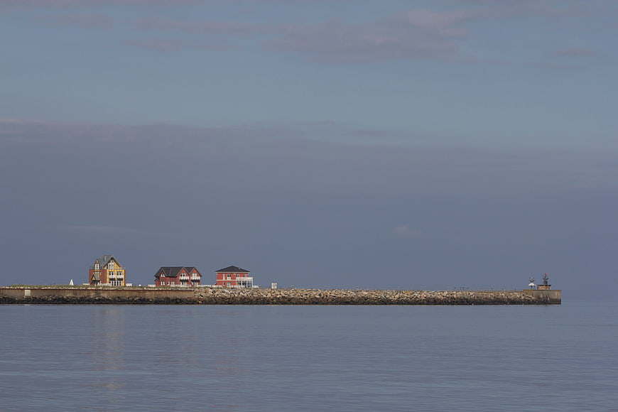 Serene coastal pier with houses and lighthouse at dusk