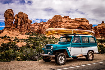 Vintage teal Jeep with wooden canoe on desert road