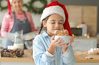 Little girl smelling gingerbread cookies in Santa hat